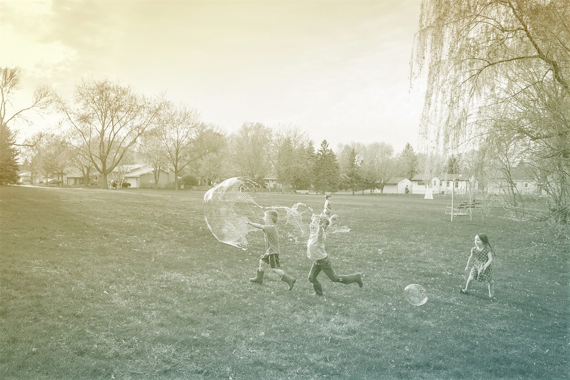 Four children chasing giant soap bubbles in a public park